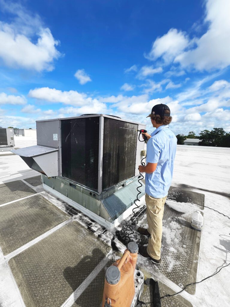 HVAC tech cleaning a condenser coil on a Southwest Florida rooftop.